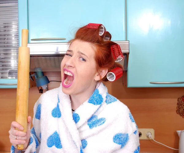 The young housewife in hair curlers in rage shouts and threatens having threatened a rolling pin