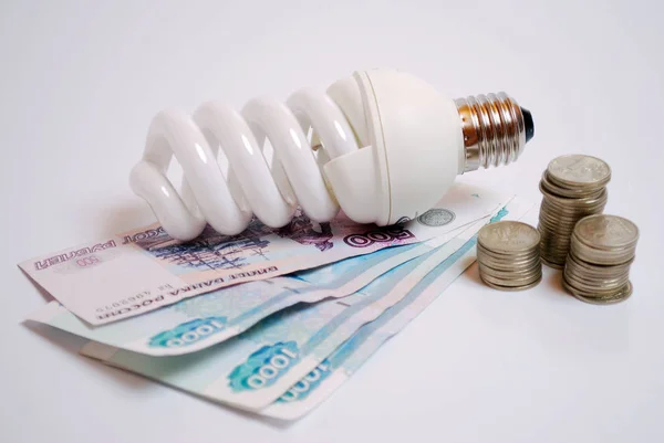 Energy-saving light bulb and money. Paper bills and coins. Saving money.