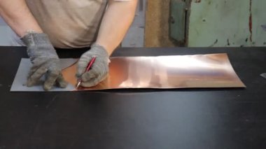 Usta kalaycı, bakır levhadan yapılmış boş bir şablona göre geleceğin ürününün detaylarını çiziyor. Üretim. El yapımı iş.