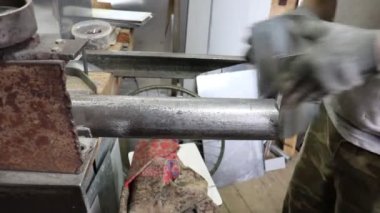 Usta Tinsmith boruya eğilir ve kilidi galvanize çelikten yapılmış gelecekteki ürünün detaylarıyla ilgili bir çekiçle devirir. Üretim. El yapımı iş.