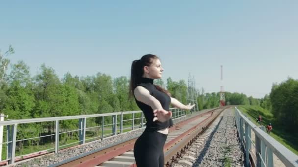 Юная брюнетка выполняет дыхательные упражнения на железнодорожном мосту через шоссе — стоковое видео