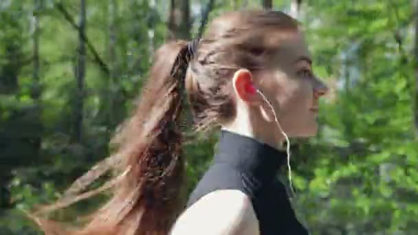 Νέοι μελαχρινή με ακουστικά που εκτελείται σε ένα δασικό δρόμο. — Αρχείο Βίντεο