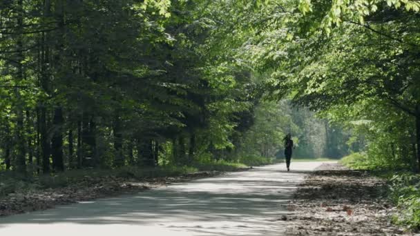 Jeune brune avec écouteurs fonctionnant sur une route forestière . — Video