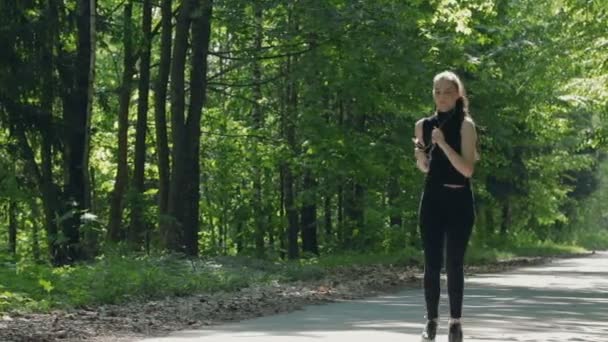 Юная брюнетка с наушниками, бегущая по лесной дороге . — стоковое видео