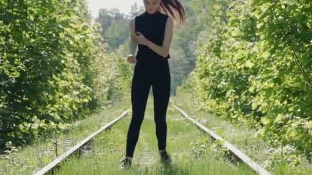 Jonge brunette in een zwart pak uitvoert fysieke oefeningen op de achtergrond van een verlaten spoor — Stockvideo