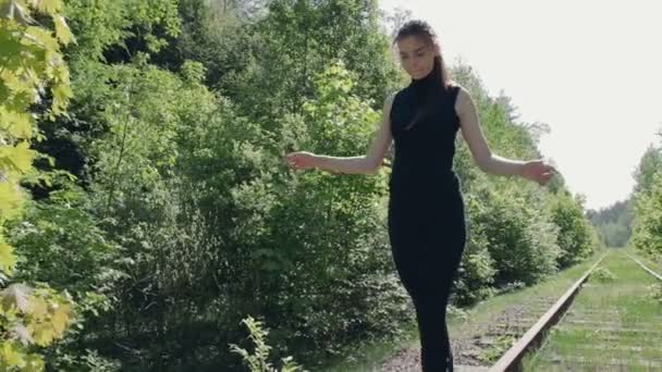 Mladá brunetka v černém obleku je na kolejnici staré železnice. Dívka drží rovnováhu — Stock video