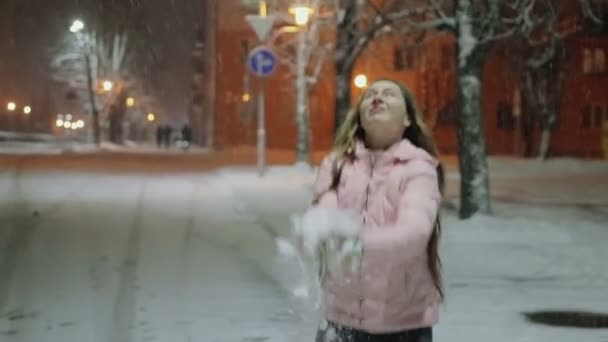 Porträtt av en ung glad kvinna i en Vinterstaden. Flickan går ner på gatan och har snön — Stockvideo