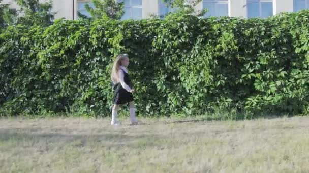Маленькая забавная школьница в школьной форме и портфеле на плечах бежит в школу — стоковое видео