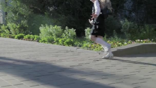 A little funny schoolgirl in school uniform and a briefcase on her shoulders runs to school — Stock Video