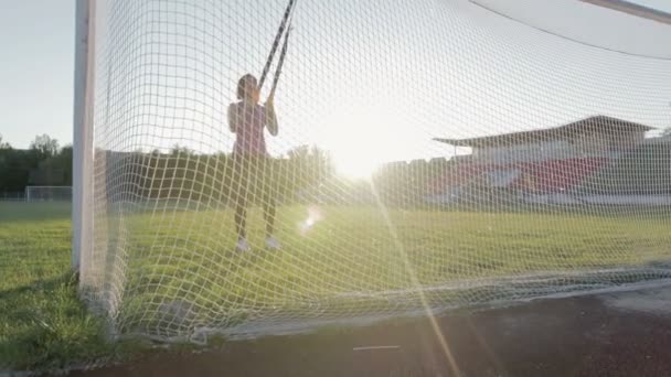 Bela menina de fitness treina no estádio. Um jovem atleta está envolvido com loops TRX no campo no gol de futebol — Vídeo de Stock