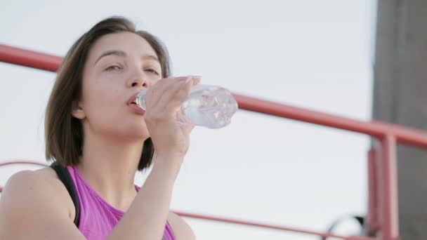 Jonge gezonde atleet drinkbaar water uit een fles zitten op het podium van het stadion — Stockvideo