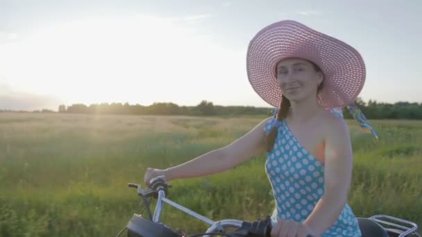 Счастливая молодая женщина в шляпе ездит на ретро мотоцикле и наслаждается поездкой по грунтовой дороге среди полей и лугов — стоковое видео
