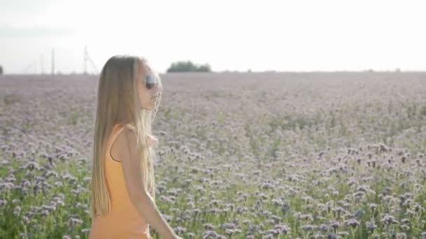 Blond, kleine meisje is dragen van een zonnebril op de achtergrond van wilde bloemen — Stockvideo