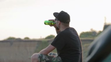 Kaygısız, Genç, dost erkek deniz kaya oturur ve içecekler bira.