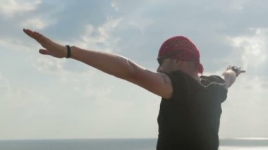 Kaygısız, Genç adam uçurumdan denizden üzerinde duruyor ve sahiptir. O elleri yayılmış, Rüzgar onu getirmiş. Mutlu ve dostane biri. O siyah t-shirt ve şort giymiş.