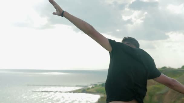 Zorgeloos, jonge, minnelijke dude staat op een klif boven de zee en geniet. — Stockvideo