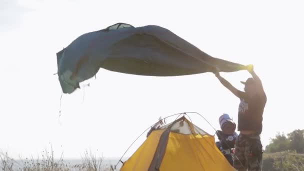 De biker zet de tent in een sterke wind in de buurt van de motorfiets enduro — Stockvideo