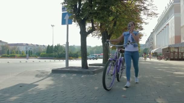 Retrato de una chica joven y feliz que pasea por la ciudad con una bicicleta y bebe café — Vídeo de stock