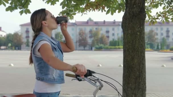 Portret van een jonge, gelukkig meisje loopt rond de stad met de fiets en drinkt koffie — Stockvideo
