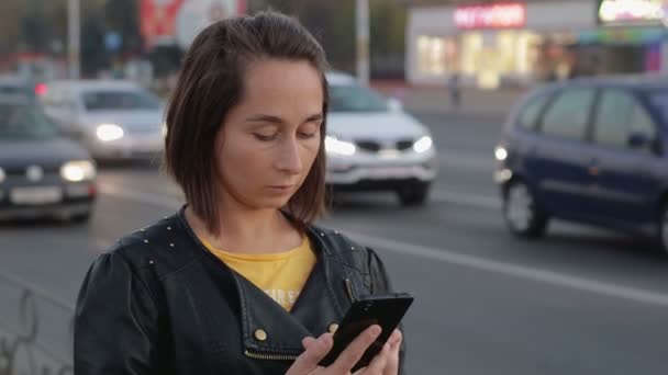 Πορτρέτο ενός νεαρού κοριτσιού που στέκεται στην πόλη, στα χέρια της ένα smartphone, κινητού τηλεφώνου — Αρχείο Βίντεο