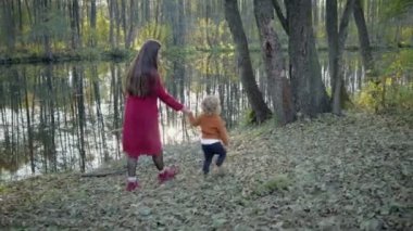 Anne ve oğlu şık giysiler içinde yakın göl sonbahar ormanın içinde yürümek, ağaçların yansıması göle görülebilir