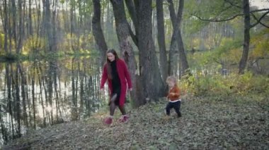 Anne ve oğlu şık giysiler içinde yakın göl sonbahar ormanın içinde yürümek, ağaçların yansıması göle görülebilir