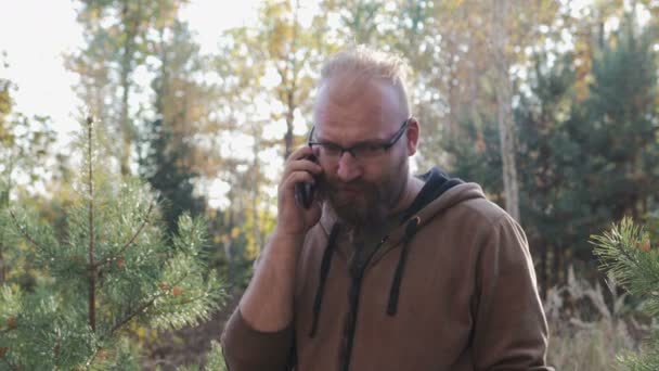 Man talar i telefon i parken, mot träden — Stockvideo