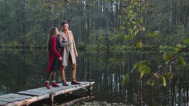 Glada, unga par stående och kramas, kyssas på träbro vid sjön — Stockvideo