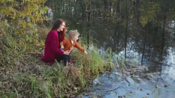 Madre e figlio seduti, parlando e abbracciandosi vicino al lago contro il paesaggio autunnale — Video Stock