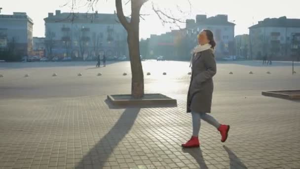 Νεαρό, όμορφο κορίτσι σε ένα παλτό και γυαλιά περπάτημα κάτω από το δρόμο της πόλης — Αρχείο Βίντεο
