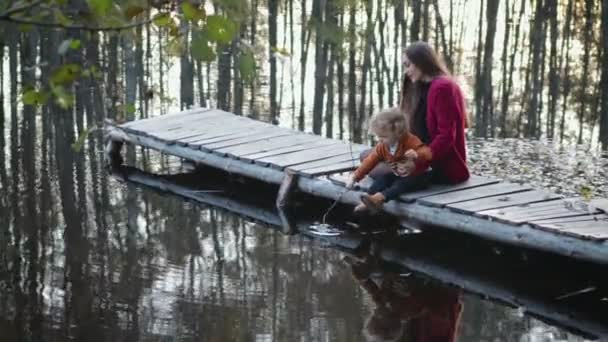 母と息子は、湖の上の木製の橋の上に座るし、美しい景色をお楽しみください。家族の概念 — ストック動画