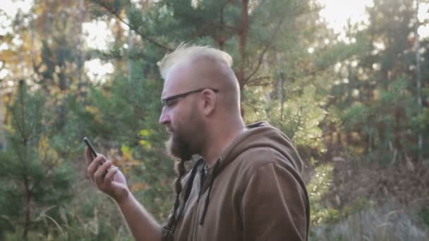 Een jonge man met een baard zweert en schreeuwt op de telefoon tegen de herfst bos — Stockvideo