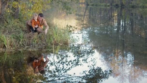 Семья сидит рядом с озером и отражается в воде — стоковое видео