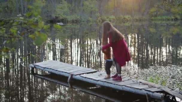 Moeder en zoon zitten en spelen op de pier in de buurt van het bos meer — Stockvideo