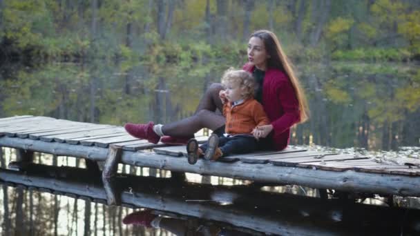 Mor och son sitta och spela på bryggan nära sjön skog — Stockvideo