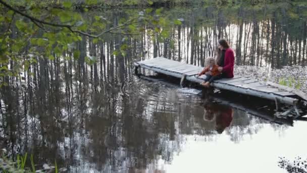 Mutter und Sohn sitzen und spielen auf der Seebrücke am Waldsee — Stockvideo