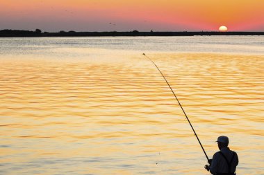 adam gün batımında sahilde balık tutuyor