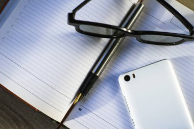 dolma kalem, smartphone ve gözlük bir defter üzerinde yalan
