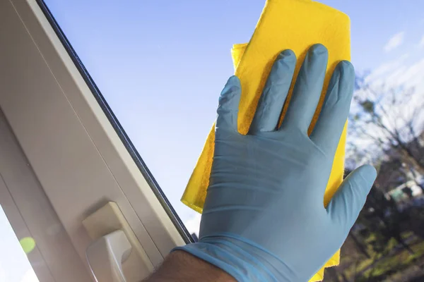 The hand in the rubber glove wipes the window with a yellow cloth