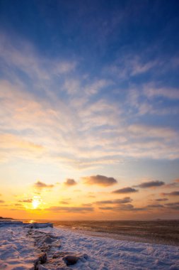 kar ve soğuk, buz kaplı deniz günbatımı sırasında altında bir plaj