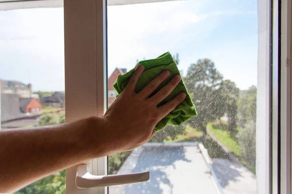 A man\'s hand washes the window with a green rag