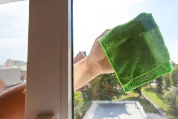 A man\'s hand washes the window with a green rag