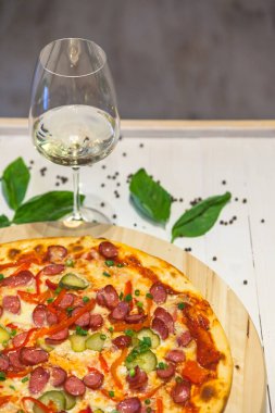 küçük sosis, fesleğen ve bir bardak beyaz şarap beyaz bir tablo ile iştah açıcı pizza