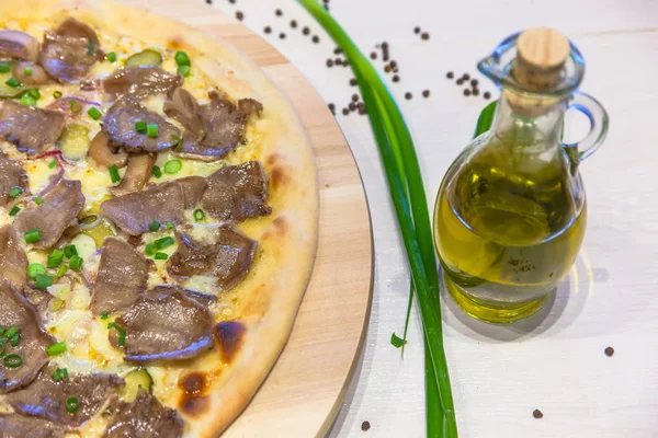 appetizing pizza with mushrooms, meat, green onions and olive oil on a white table