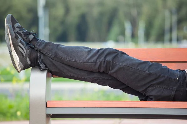 legs of a man in black jeans lying on a bench