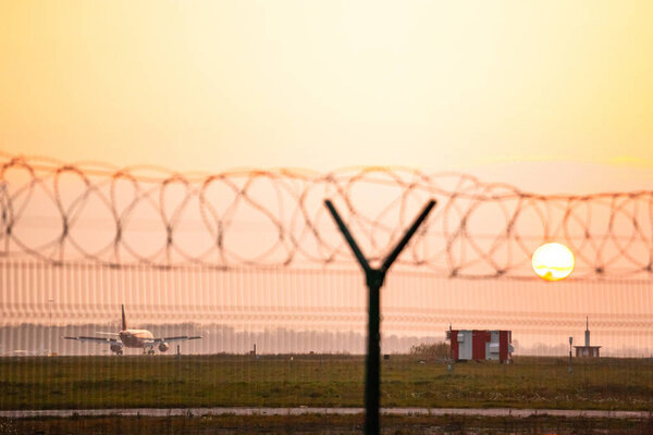 a passenger plane sat on the runway at the airport against the orange sky and the setting sun