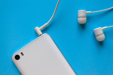 mavi arka planda bağlı beyaz kulaklıklara sahip beyaz akıllı telefon