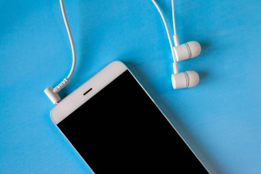 mavi arka planda bağlı beyaz kulaklıklara sahip beyaz akıllı telefon