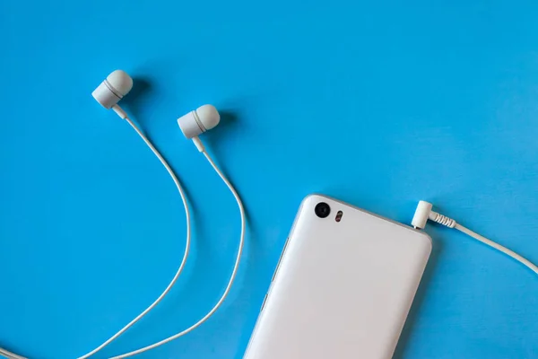 white smartphone with connected white headphones on blue background