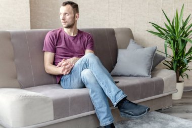 Genç sakin bir adam parlak bir odada bir koltukta oturur ve pencereden dışarı bakar.